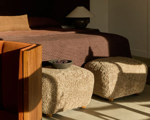 Modern bedroom with a bed, ottomans, and a lamp.